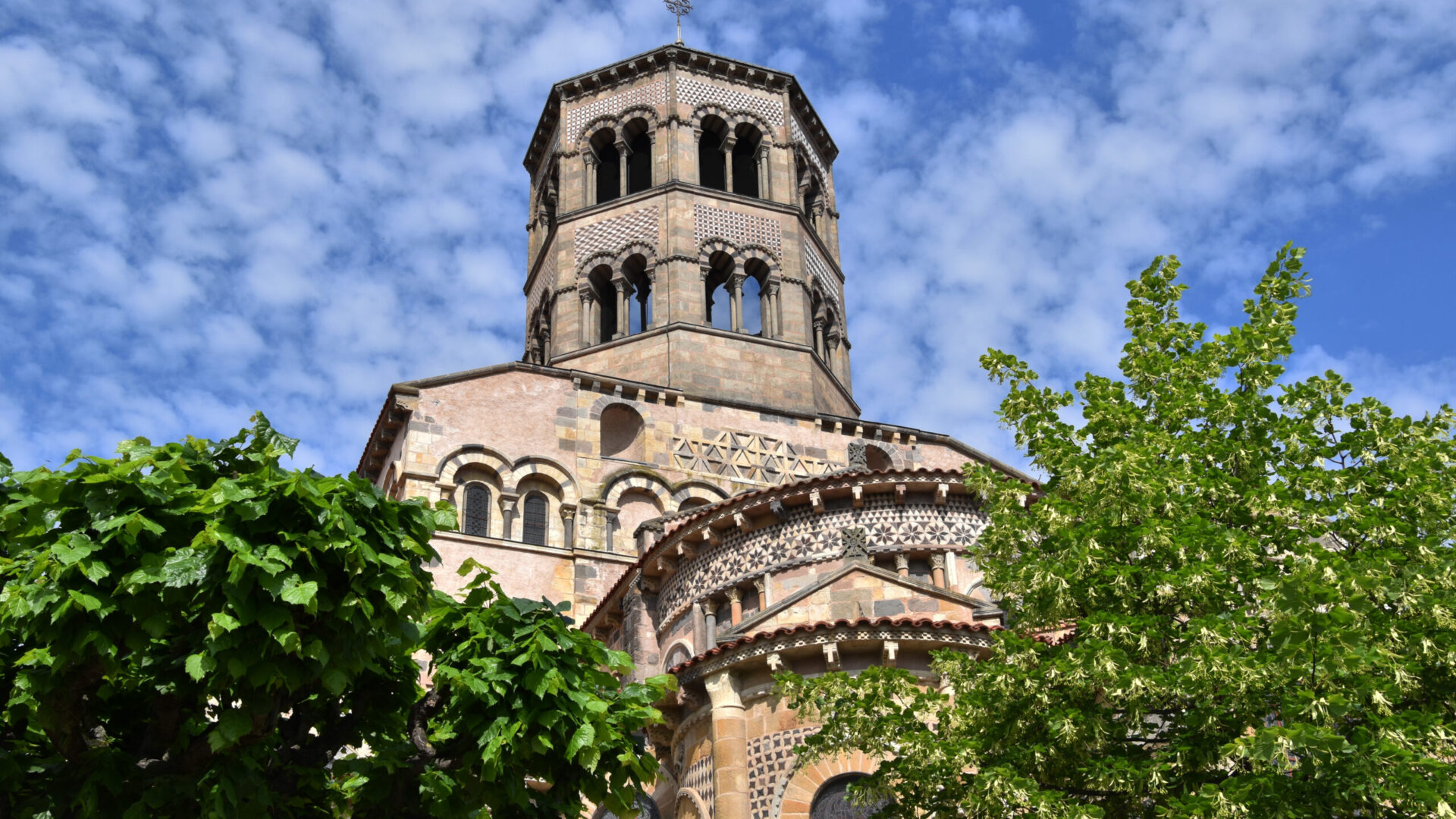 photo prise du sol du clocher d'une grande église romane, qui dépasse allègrement les deux arbres qui lui fond face